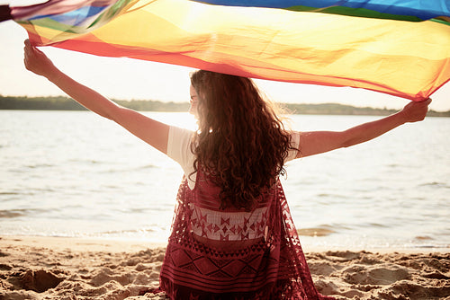 Rear view of woman with rainbow flag on the beach