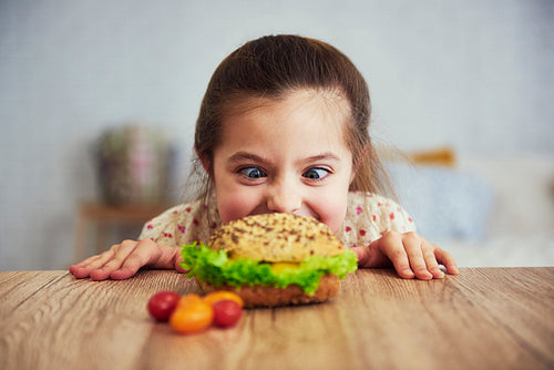Playful girl looking at delicious hamburger