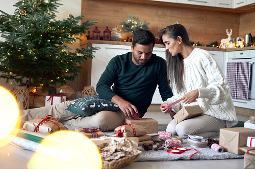 Multi ethnicity couple packing Christmas present together at home