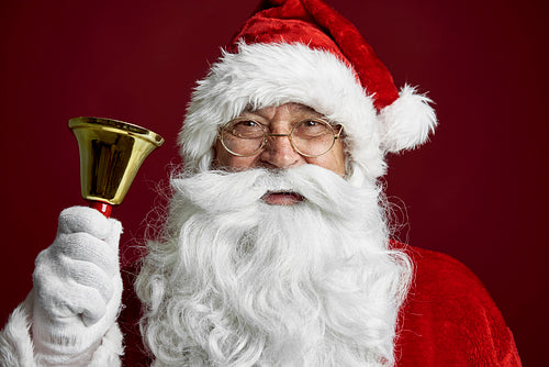 Close up of caucasian Santa Claus on red background and holding a golden bell