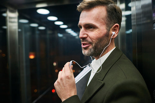Side view of happy businessman listening to music in elevator