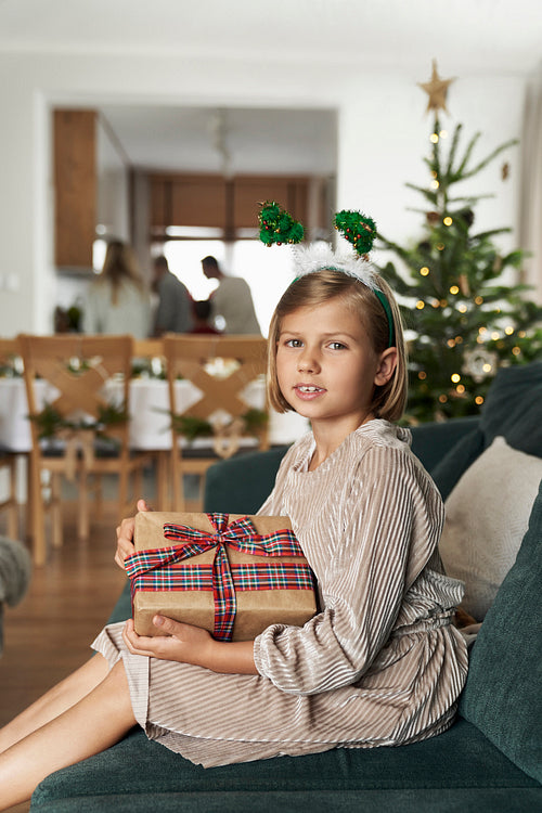 Portrait of caucasian girl holding Christmas gift while sitting on sofa