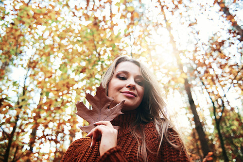 Beautiful smiling young woman holding autumnal leaf