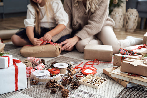 Christmas decorations on foreground and girl and mother wrapping Christmas gifts on floor in the background