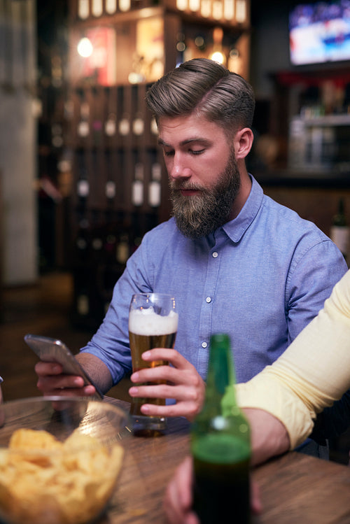 Hipster man using mobile phone and drinking beer