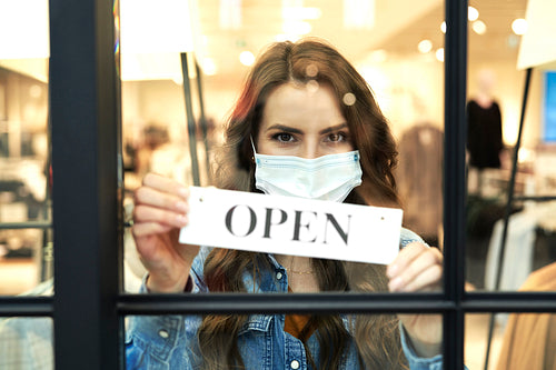 Woman in protective mask holding open sign in store window