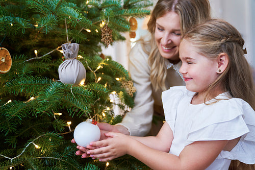 Cute girl decorating the Christmas tree with mum