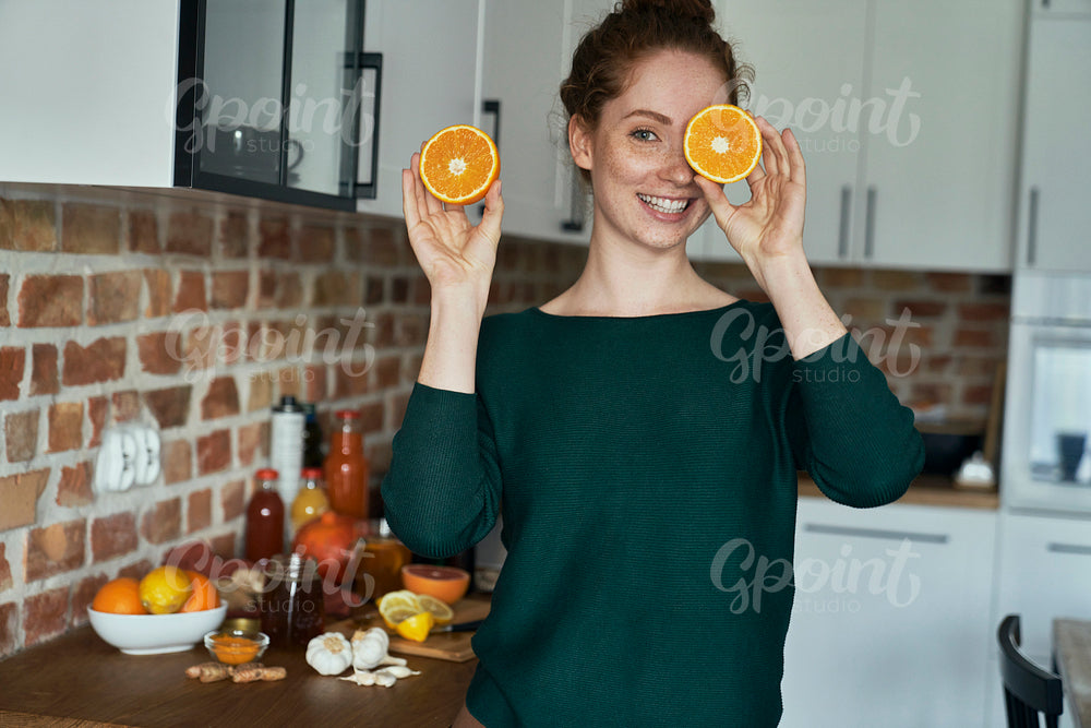 Caucasian young woman covering eyes with orange halves 
