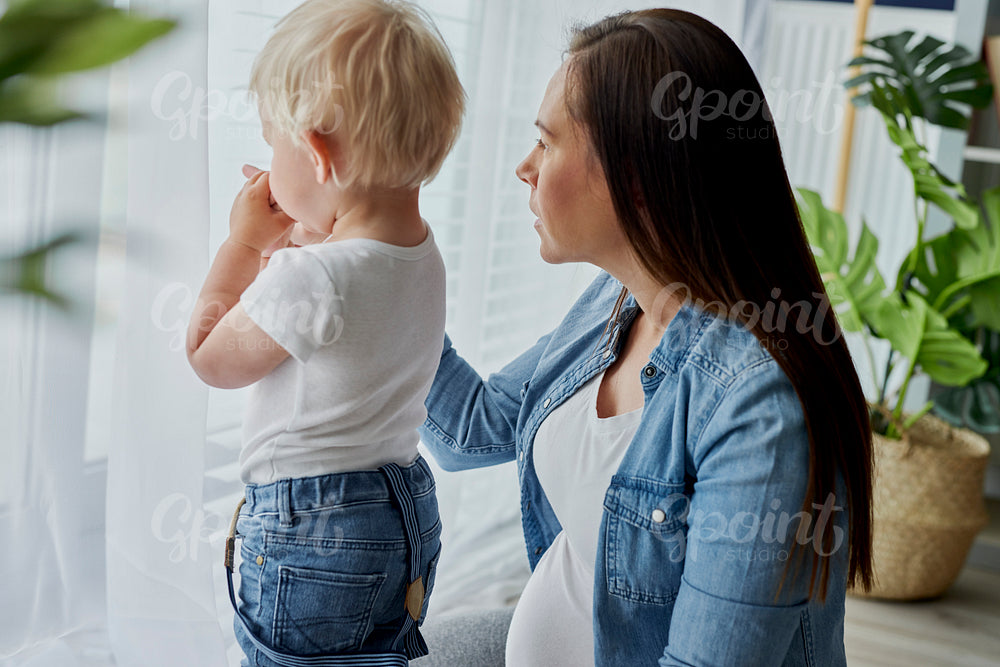 Woman and her toddler son standing next to the window