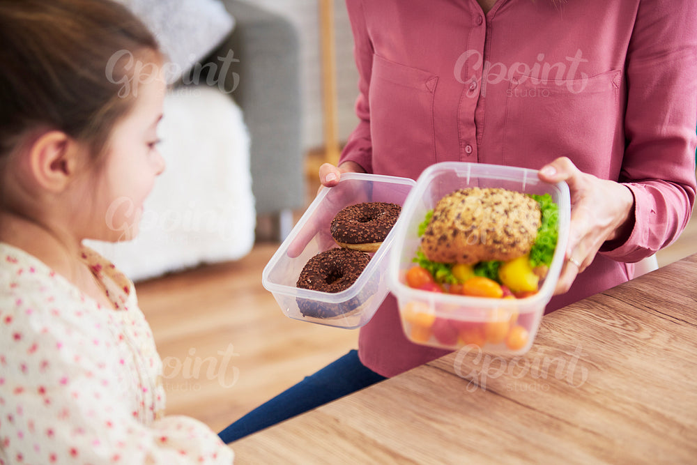 Young child choosing between healthy sandwich and chocolate donuts