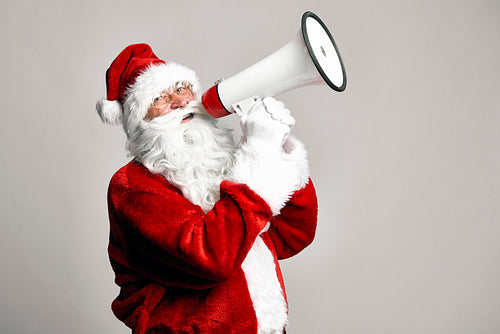 Caucasian Santa Claus talking by megaphone on grey background