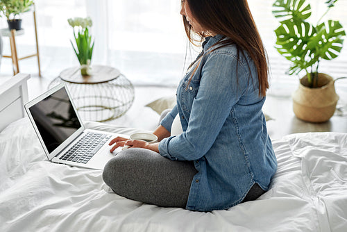 Pregnant woman using a computer while sitting on bed
