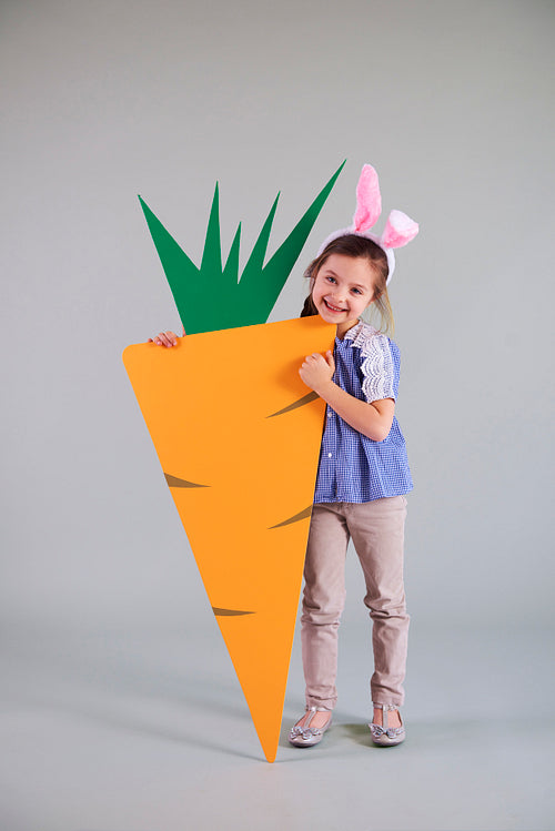 Portrait of child in easter bunny costume holding big carrot
