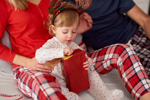 Baby girl opening Christmas gift with parents in Christmas morning
