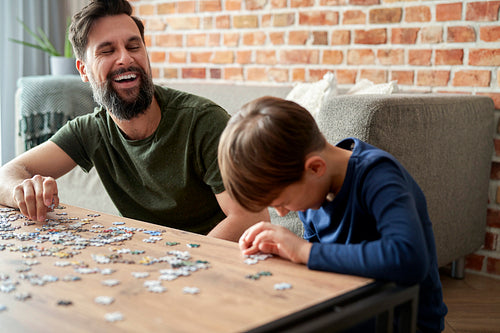 Happy son and father having fun during solving jigsaw puzzle