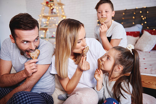 Playful family eating gingerbread cookies in bed
