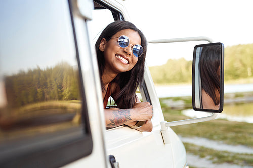 Cheerful mixed race woman  sticking out of camper's window and looking at camera