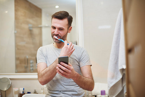 Man brushing his teeth and using mobile phone