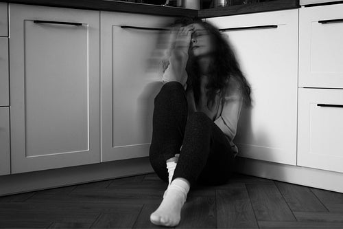 Black and white image of thoughtful young caucasian woman sitting on floor in the kitchen