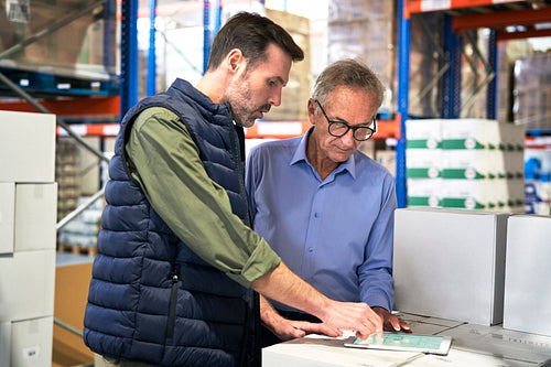 Two caucasian men in mature age discussing over digital tablet in warehouse