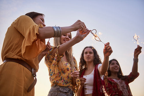 Four young women with burning sparklers during sunset