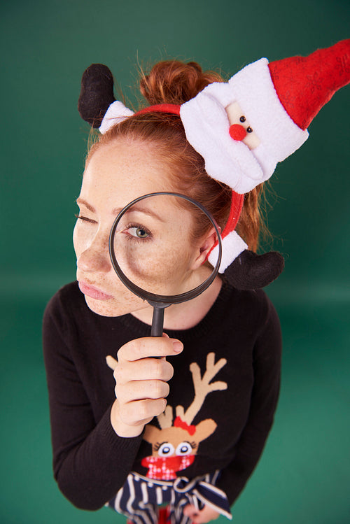 Funny girl in christmas clothes looking through magnifying glass